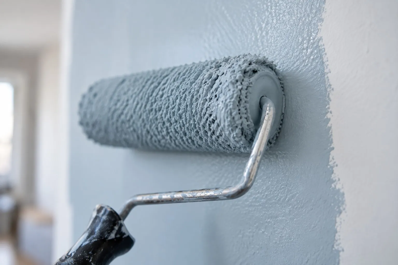 Detalle de un rodillo aplicando pintura gris azulada en una pared